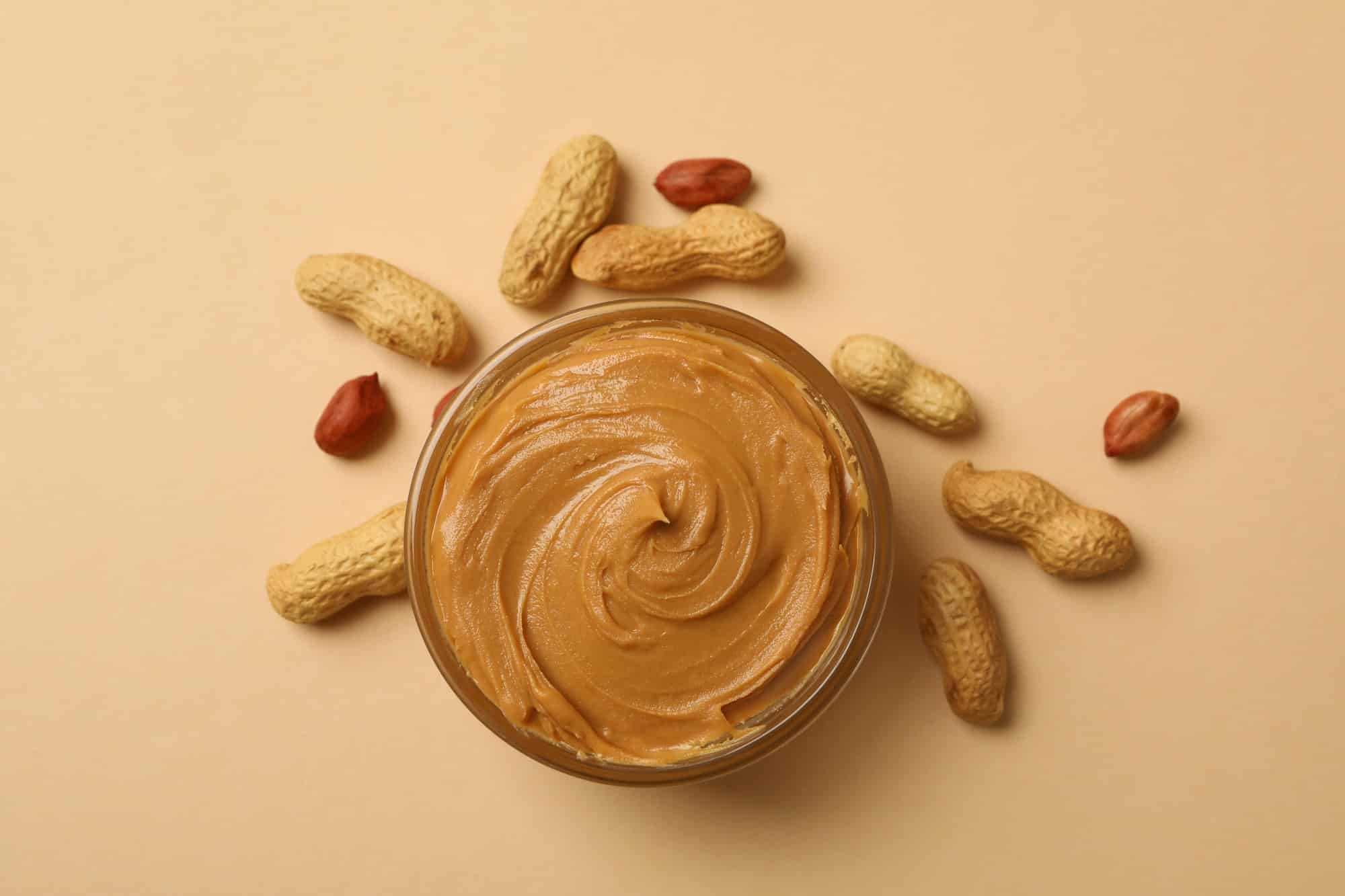 Peanut and bowl with peanut butter on beige background