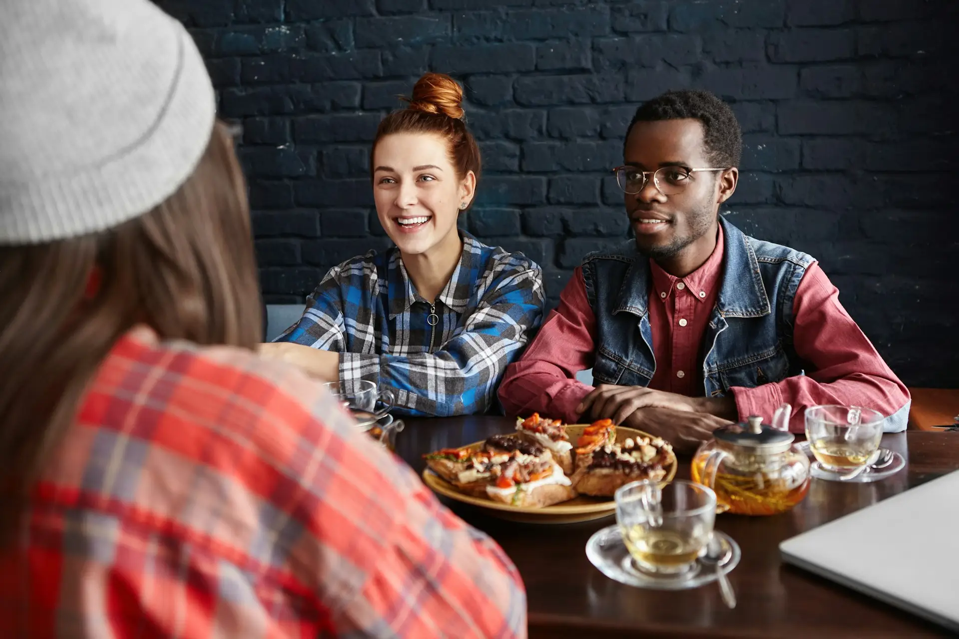 International friendship. Fashionable African male in glasses sitting at cafe table with food next t